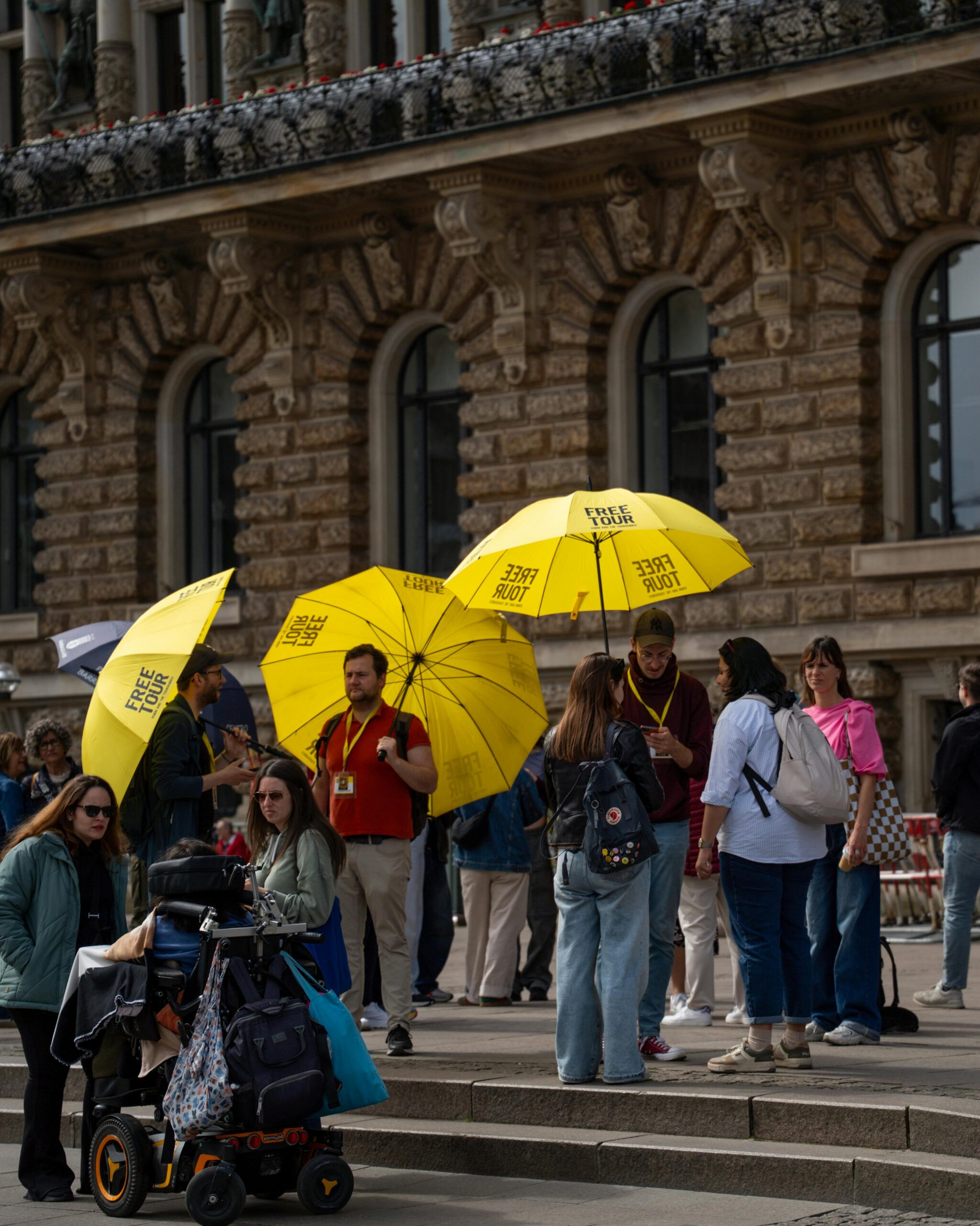 Menschen versammeln sich vor einem Steingebäude und halten gelbe "FREE TOUR"-Regenschirme in der Hand, die sich ideal für digitale Visitenkartenplattformen mit QR-Code/NFC eignen. | GetinTouch.ID